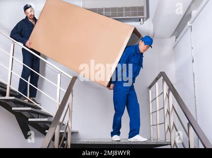Professionelle Arbeiter, die Kühlschränke auf Treppen in Gebäuden tragen Stockfoto