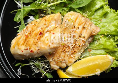 Leckerer gegrillter Fisch mit Zitrone auf dem Teller, Nahaufnahme Stockfoto