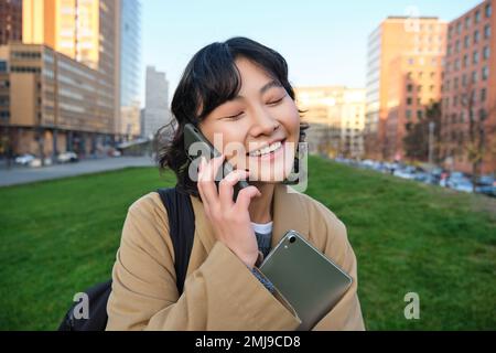 Universitätsleben. Junge asiatische Schülerin, Mädchen mit Tablet und Notebook, spricht auf der Straße über Handy, während sie vom Campus spaziert Stockfoto