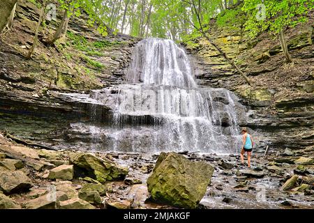 Eine junge Frau kühlt die Sommerhitze im Sommer in einem Wasserfall ab Stockfoto