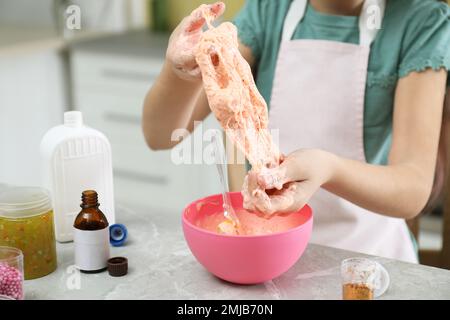 Kleines Mädchen, das Heimwerker-Schleim-Spielzeug am Tisch in der Küche knete, Nahaufnahme Stockfoto