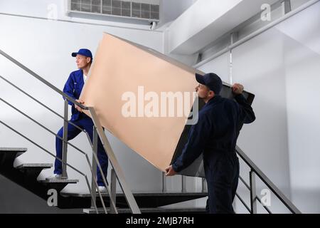 Professionelle Arbeiter, die Kühlschränke auf Treppen in Gebäuden tragen Stockfoto