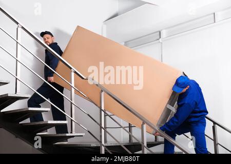 Professionelle Arbeiter, die Kühlschränke auf Treppen in Gebäuden tragen Stockfoto