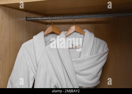 Frische weiße Bademäntel hängen in einem Holzschrank Stockfoto