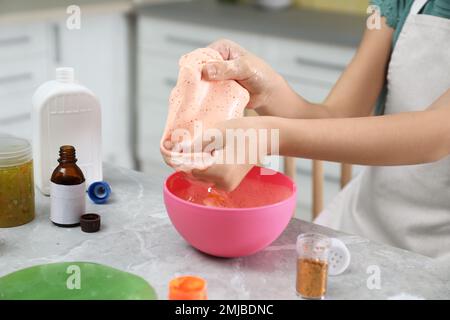 Kleines Mädchen, das Heimwerker-Schleim-Spielzeug drinnen am Tisch knete, Nahaufnahme Stockfoto