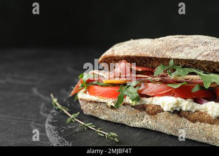 Köstliches Sandwich mit frischem Gemüse und Prosciutto auf schwarzem Tisch, Nahaufnahme. Platz für Text Stockfoto