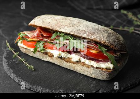 Köstliches Sandwich mit frischem Gemüse und Prosciutto auf dem schwarzen Tisch Stockfoto