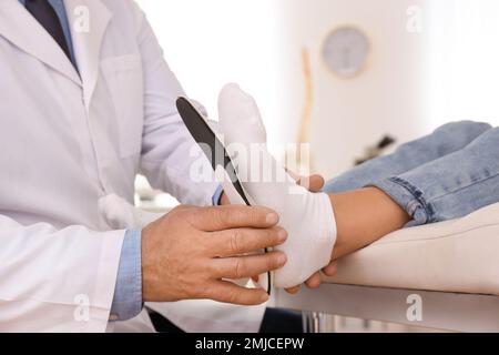 Die Einlegesohle des männlichen Orthopäden am Fuss des Patienten in der Klinik, Nahaufnahme Stockfoto