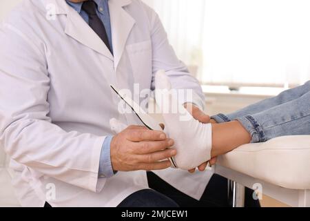 Die Einlegesohle des männlichen Orthopäden am Fuss des Patienten in der Klinik, Nahaufnahme Stockfoto