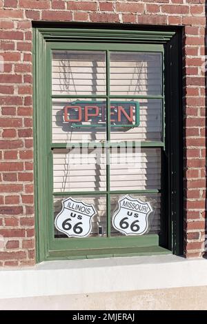 Am Fenster des Mother Road Museum in Barstow, Kalifornien, befinden sich ein offenes Neonschild und zwei US 66-Schilder, eines für Illinois und eines für Missouri. Stockfoto