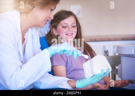 Sie beraten, wie sie sich regelmäßig weiterbehandeln lassen kann. Eine Zahnärztin, die ihrem jungen Patienten beibringt, wie man sich die Zähne putzt. Stockfoto