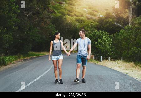 Seelenkameraden haben denselben Richtungssinn. Ein glückliches junges Paar, das draußen eine Straße entlang läuft. Stockfoto