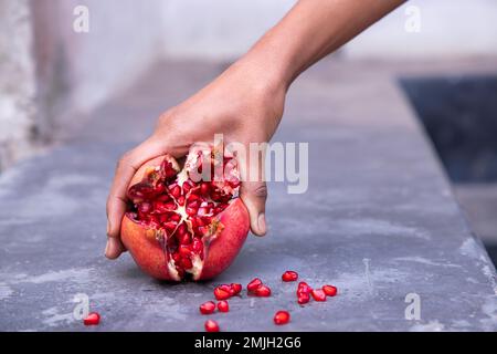 Reife Granatapfelfrucht in Frauenhand auf Betonhintergrund Stockfoto