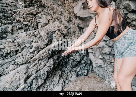 Sportlerin Klettert Auf Den Felsen. Junge Frau mit schlankem Körper klettert in einer vulkanischen Basalthöhle mit wunderschönem Blick auf das Meer. Das Sportlermädchen trainiert Stockfoto