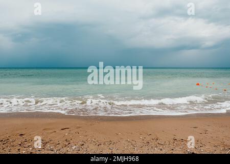 Bewölkter Himmel an regnerischen Tagen mit schaumigen Wellen, die in Richtung goldener Sandstrände bei schwachem, warmem Sonnenlicht Rollen. Niemand. Urlaubskonzept. Abstrakt Stockfoto