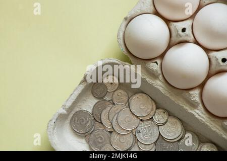 Hühnereier in Verpackungen und ukrainisches Penny-Geld auf isoliertem Hintergrund. Platz für Text Stockfoto