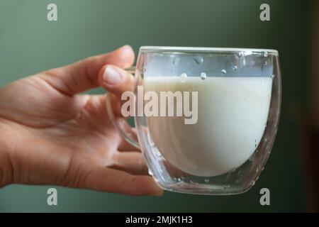 Ein junges ukrainisches Mädchen hält morgens einen durchsichtigen Glasbecher mit Milch Stockfoto