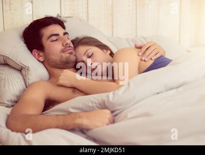 Er schläft fest in seinen Armen. Ein liebevolles junges Paar, das zusammen im Bett schläft. Stockfoto