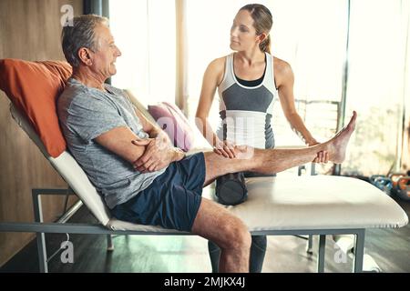Die Führung ihrer Patientin bei therapeutischen Übungen. Ein älterer Mann wird von einem Physiotherapeuten behandelt. Stockfoto
