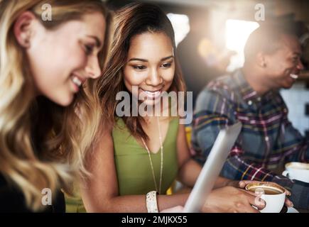 Technologie, die Menschen näher bringt. Zwei Freunde, die ein Tablet benutzen, während sie in einem Café Kaffee trinken. Stockfoto