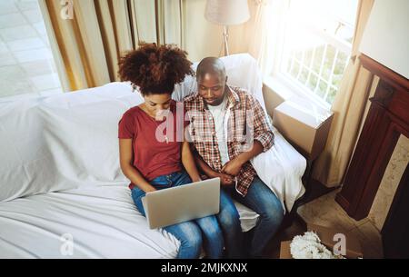 Sehen Sie sich einige Innenausstattungen für ihren Wohnraum an. Ein junges Paar, das einen Laptop benutzt, während es in sein neues Zuhause zieht. Stockfoto