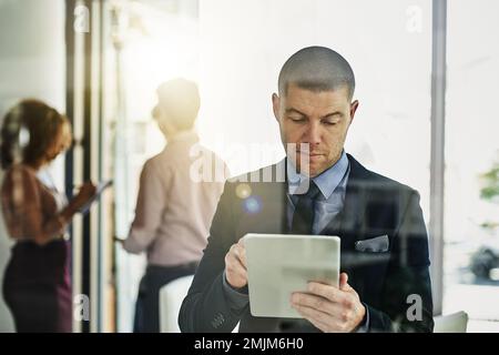 Die letzten Schliffe auf seine Präsentation. Ein Geschäftsmann, der sein Tablet verwendet, während einige Kollegen im Hintergrund sprechen. Stockfoto