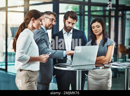 Technologie in eine Produktivitätsmaschine verwandeln. Eine Gruppe von Kollegen, die gemeinsam ein Notebook in einem modernen Büro verwenden. Stockfoto