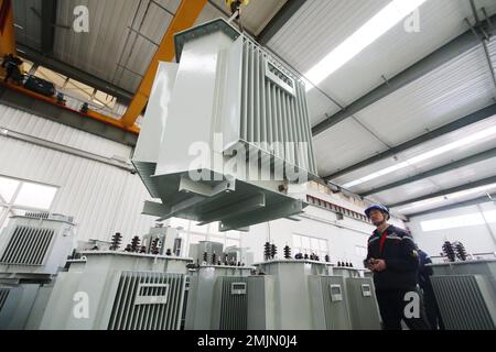 HANDAN, CHINA - 28. JANUAR 2023 - Arbeiter heben Transformatoren in einer Werkstatt von Hebei Gaojing Electric Equipment Co LTD in Handan, Nordchina Hebei p Stockfoto