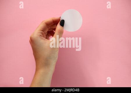 Die weibliche Hand hält einen runden Aufkleber auf pinkfarbenem Hintergrund. Modellaufkleber Stockfoto