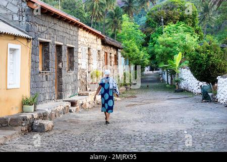 Einheimische Frau, die auf einer Rua Banana Straße mit traditionellen Häusern aus Stein im historischen Dorf cidade velha auf der Insel santiago, cabo verde, spaziert Stockfoto