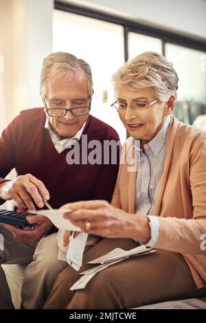 Kleine Änderungen können zu großen Einsparungen führen. Ein älteres Ehepaar, das ein Budget ausarbeitet, während es auf dem Sofa im Wohnzimmer sitzt. Stockfoto