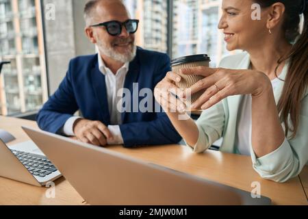 Fröhliche Frau im Business-Anzug, die eine Kaffeepause mit einem Kollegen macht Stockfoto
