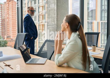Zwei Bürokollegen in schönen Anzügen, die am Arbeitsplatz Blicke austauschen Stockfoto