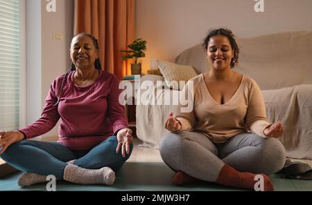 Glückliche kleine Tochter mit ihrer Mutter, die zu Hause Yoga macht Stockfoto