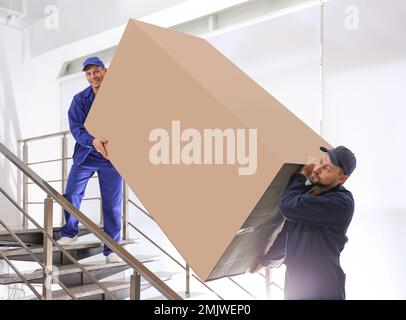 Professionelle Arbeiter, die Kühlschränke auf Treppen in Gebäuden tragen Stockfoto