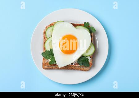 Teller mit leckerem Sandwich mit herzförmigem Spiegelei auf hellblauem Hintergrund, Draufsicht Stockfoto