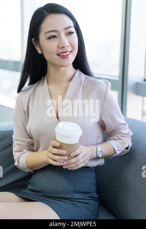 Junge Geschäftsfrau im Büro trinkt Kaffee Stockfoto