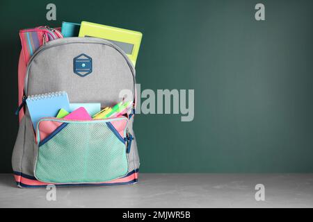 Eleganter Rucksack mit verschiedenen Schreibwaren auf dem Tisch an der Tafel. Platz für Text Stockfoto