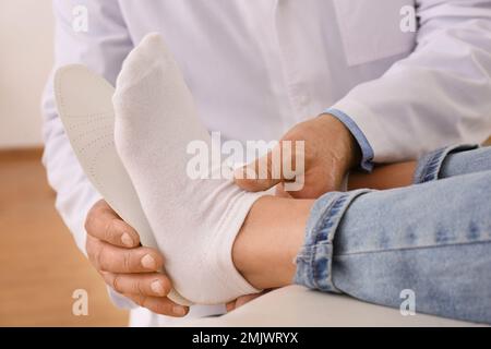 Die Einlegesohle des männlichen Orthopäden am Fuss des Patienten in der Klinik, Nahaufnahme Stockfoto