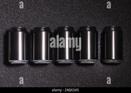 Foto von fünf schwarzen, leeren Aluminiumdosen hintereinander auf schwarzem Hintergrund mit Glitzereffekt Stockfoto