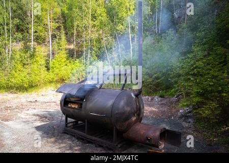 Ein riesiger Holzraucher steht an einem sonnigen Sommertag am Waldrand Stockfoto