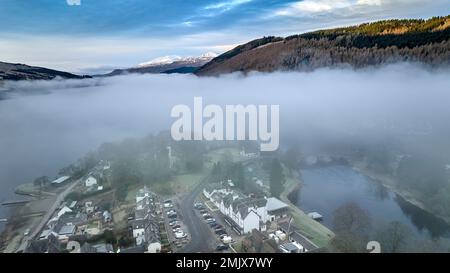 Blick aus der Vogelperspektive auf das Dorf Kenmore auf Loch Tay mit Kenmore Bridge (1774) an einem nebeligen Wintermorgen. Der schneebedeckte Ben Lawers taucht in der Ferne auf. Stockfoto