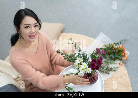 Die junge Frau zu Hause, die Blumen arrangiert Stockfoto