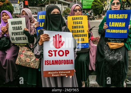 Bogor, Indonesien. 27. Januar 2023. Indonesische muslimische Frauen halten während eines Protests gegen Schwedisch-Dänisch ein Plakat, um die jüngste Entweihung des heiligen islamischen Buches Koran durch einen rechtsextremen Politiker Rasmus Paludan in Bogor, West-Java, Indonesien, am 27. Januar 2023 anzuprangern. Die globale islamische Gemeinschaft verurteilte Islamfeindlichkeit, nachdem der schwedisch-dänische rechtsextreme Politiker Rasmus Paludan bei einer Kundgebung in Stockholm am 21. Januar eine Kopie des Korans verbrannte. (Foto: ANDI M RIDWAN/INA PHOTO AGENCY/SIPA USA) Guthaben: SIPA USA/Alamy Live News Stockfoto