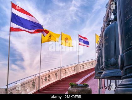 Thailändische Nationalflaggen, buddhistische und thailändische Königsflaggen an der roten Treppe und Glocken am blauen sonnigen Himmel. Stockfoto