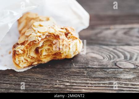 Frisches, leckeres Croissant in weißer Papiertüte auf dem Tisch. Rustikaler Holzhintergrund mit süßem Dessert. Frühstück oder Mittagessen. Stockfoto