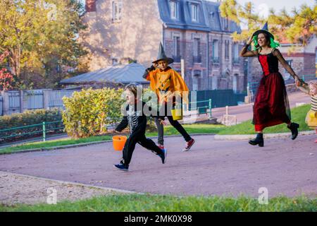 Eine Familie mit Jungs, die in Halloween-Verkleidung läuft und Süßigkeiten-Eimer hält Stockfoto