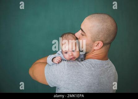 Junger Vater mit kurzen Haaren küsst seine neugeborene Tochter Stockfoto