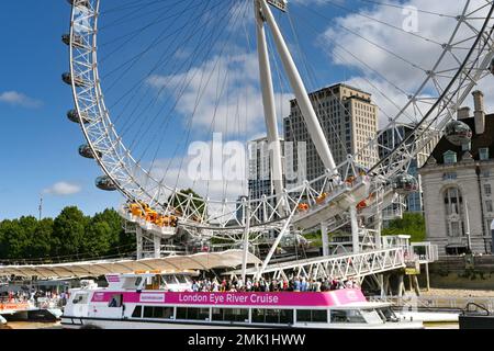 London, Großbritannien - August 2022: Touristenboot auf dem Fluss mit Passagieren auf dem Oberdeck, das am London Eye auf der Themse festgemacht ist Stockfoto