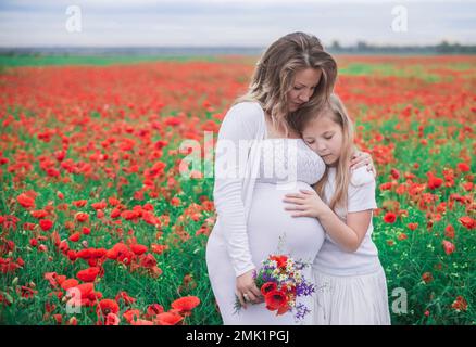 Schwangere Mutter mit ihrer ältesten Tochter im Mohnfeld Stockfoto